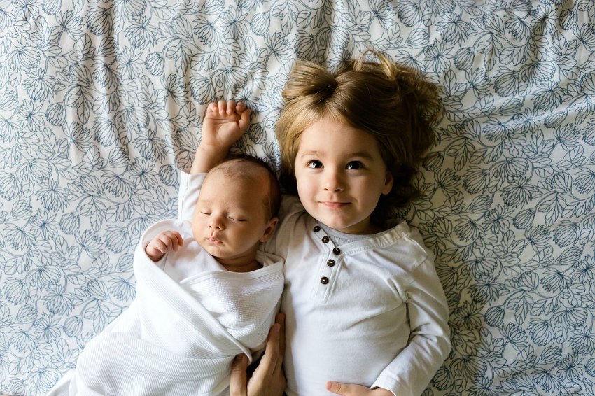 a baby and a toddler lying on a bed