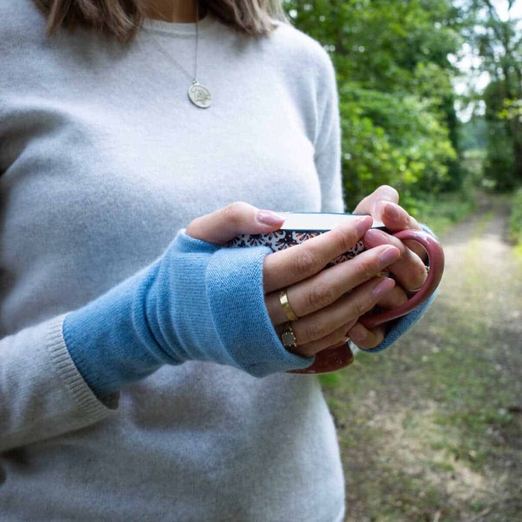 Person wearing blue fingerless gloves, holding a cup of tea.