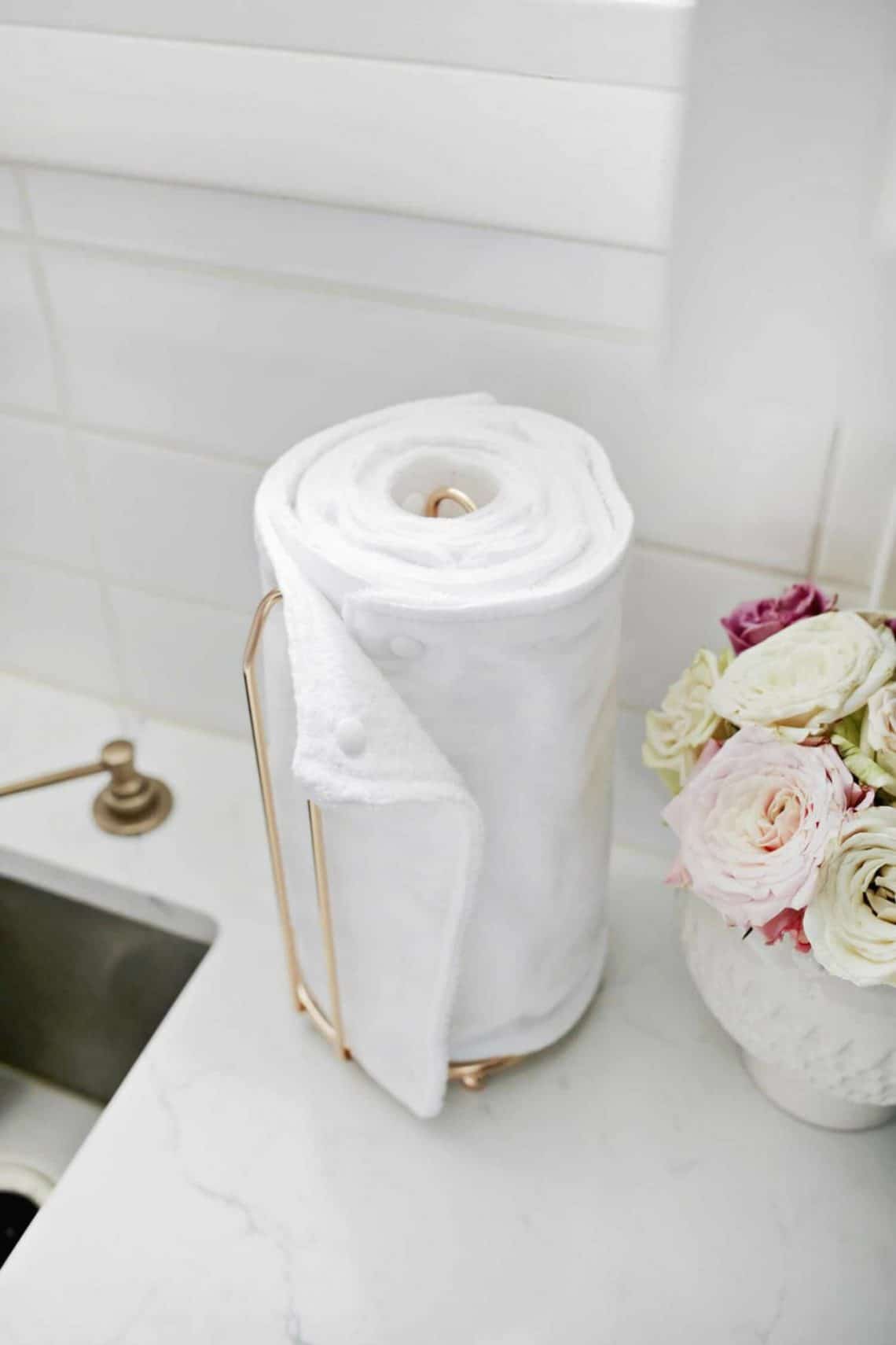 Reusable kitchen roll on a gold holder in a white tiled kitchen.