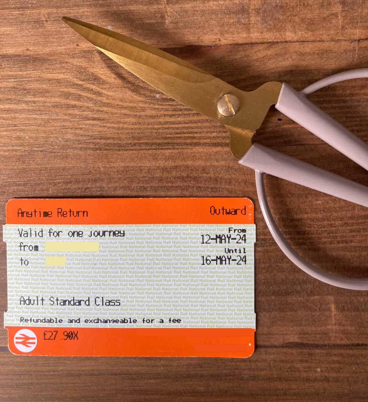 Orange train ticket on a wooden desk next to a pair of scissors,