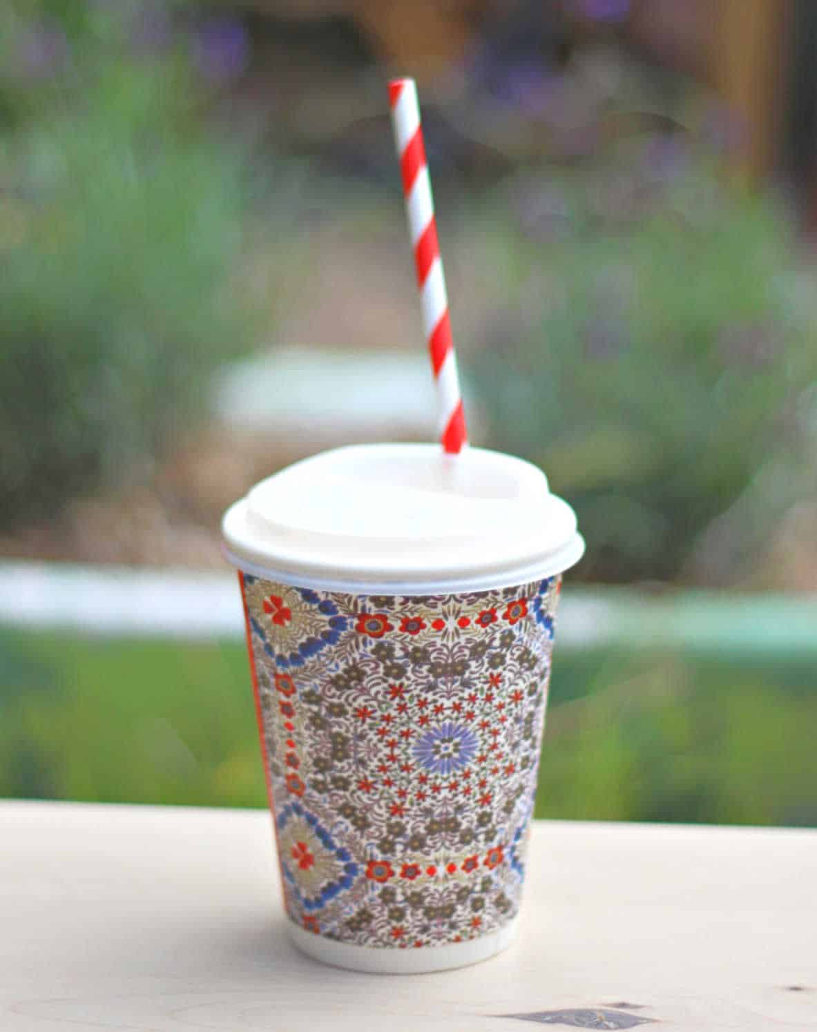 Floral disposable cup with a lid and red and white straw sticking out of it.