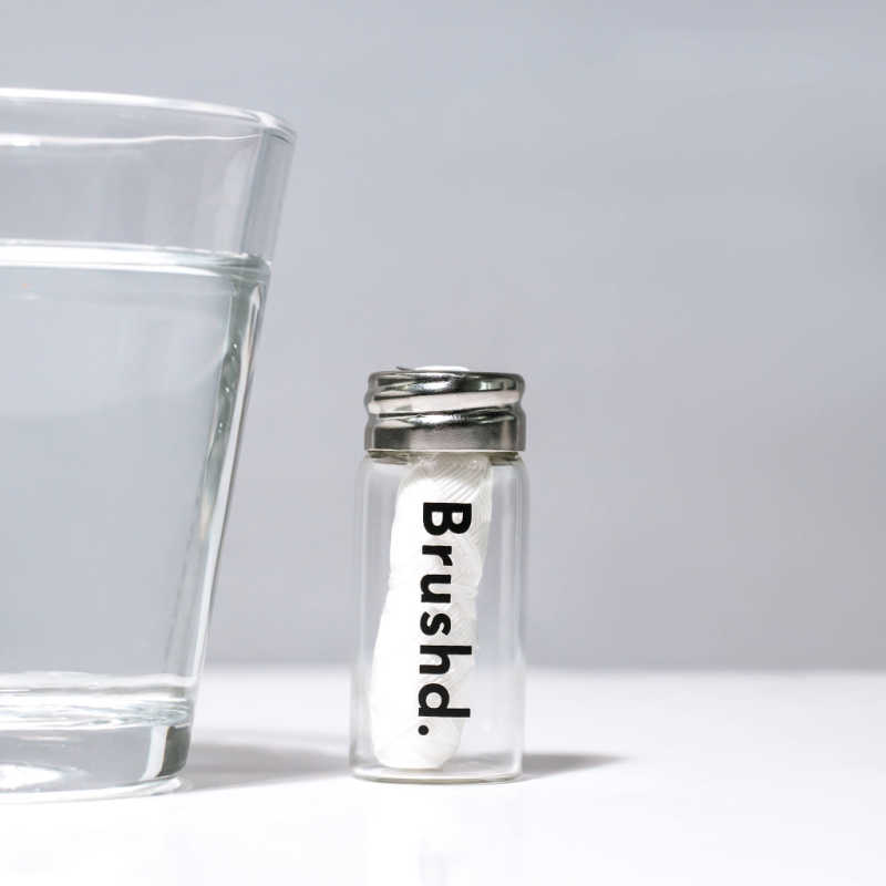 a jar of brushd floss next to a glass of water