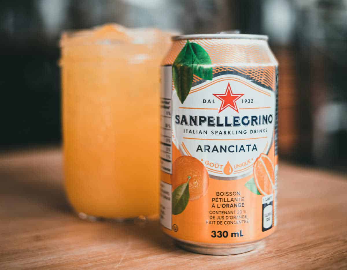 Can of orange sanpellegrino on a table next to a filled glass