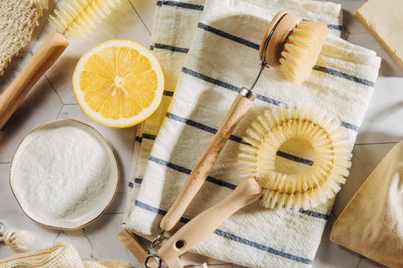 Scrubbing brushes on a dish towel, next to a halved lemon and a bowl of baking soda.